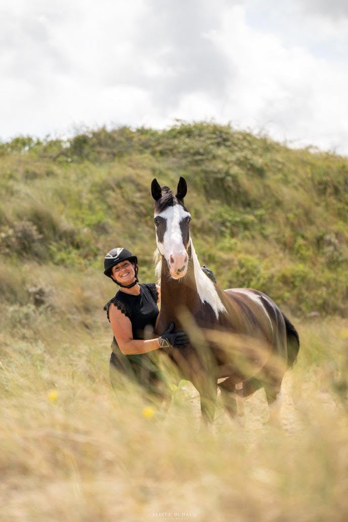 Photo de Séverine, ambassadrice de Libellule Graphisme, aux côtés de son cheval Lucky Boy des Weppes, un welsh part bred black tobiano. Lucky apparaît libre et sauvage, tandis que Séverine porte une bombe d’équitation et une tenue noire, illustrant leur duo complice et authentique.